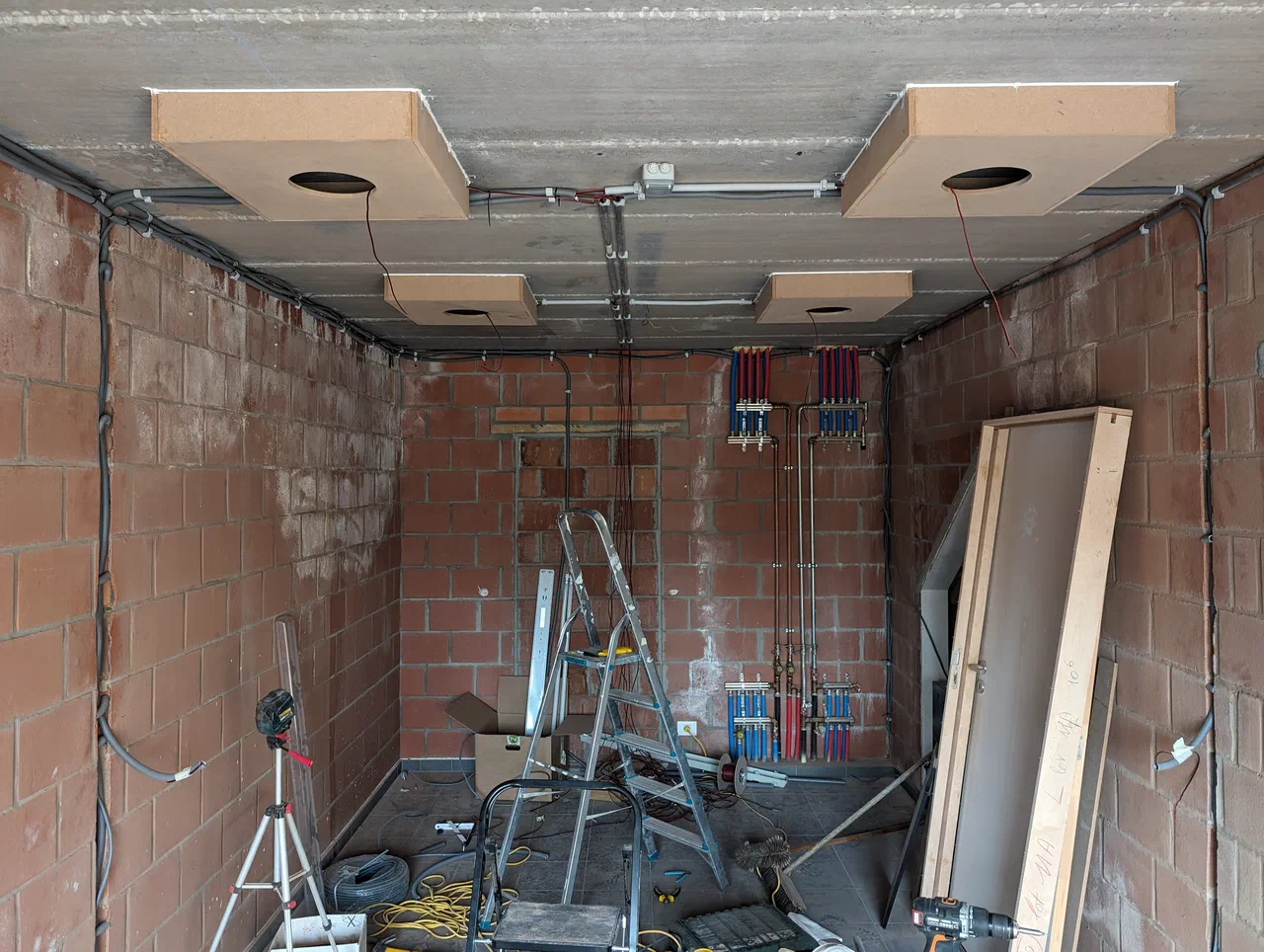 Garage renovation in progress, wooden boxes mounted against ceiling. a ladder on the floor and cables cut into bare wall