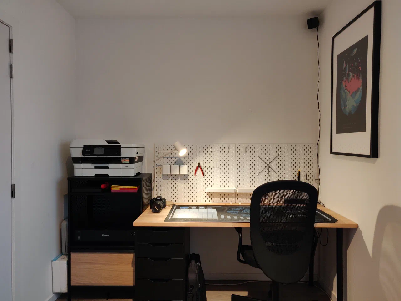 A cabinet with a printer on top and an empty desk with pegboards and a protective mat
