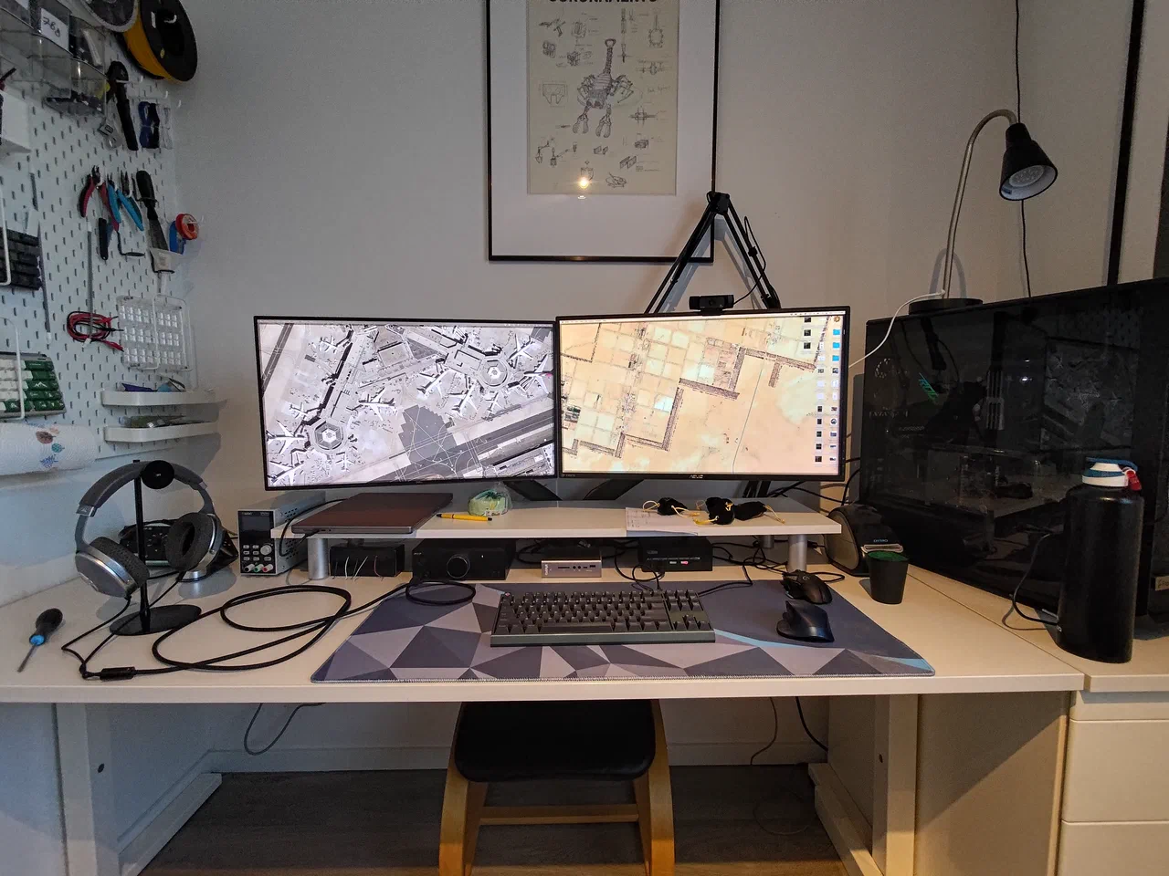 A desk with two monitors, a desktop pc to the right of it. On the left wall, tools for electronics work